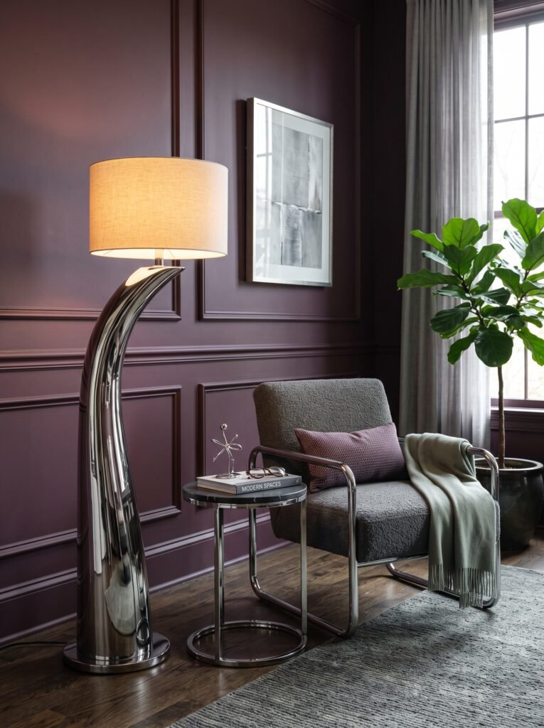 Elegant chrome interior with a sculptural chrome lamp, upholstered chrome chair, chrome side table, dark stone, and deep plum accents.