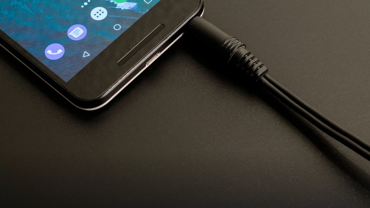 Phone connected to a charging cable — using cheap uncertified cables is one of the mistakes that age batteries faster