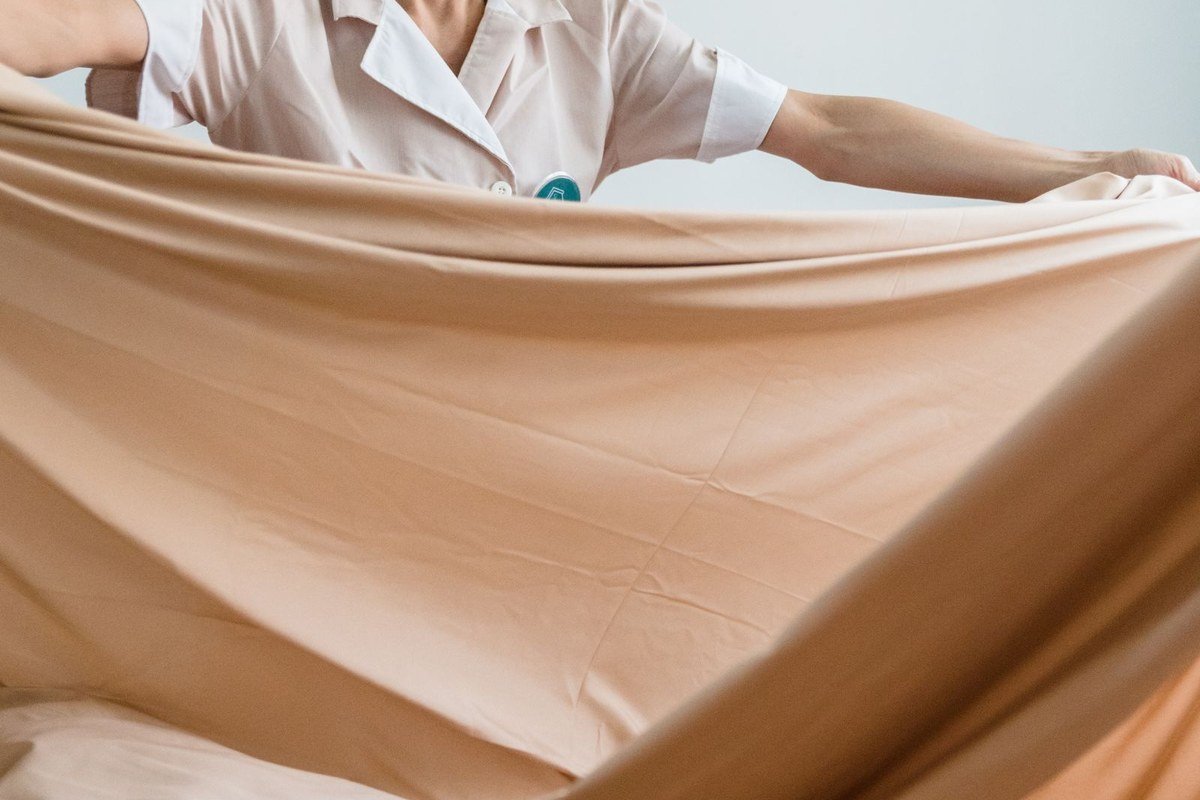 Close-up of hands tucking the elastic corners of a fitted sheet together.