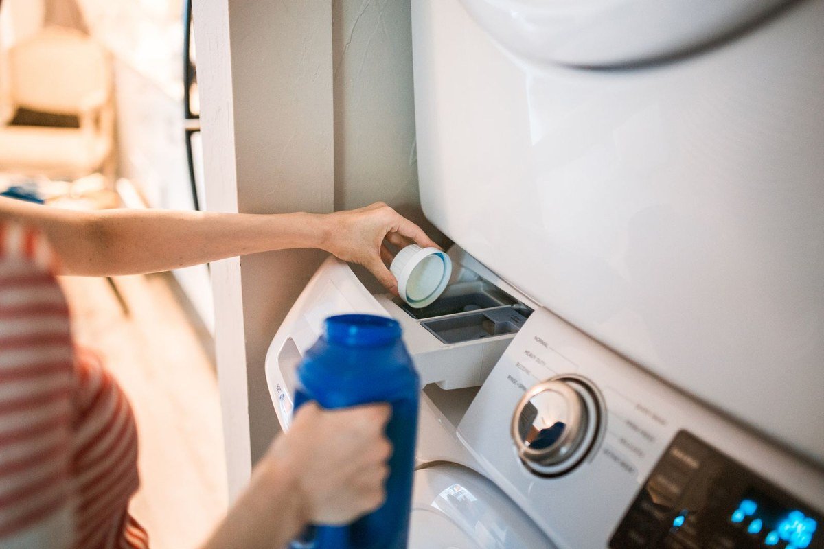 Person pouring laundry detergent into a washing machine — excess detergent leaves residue that traps odor