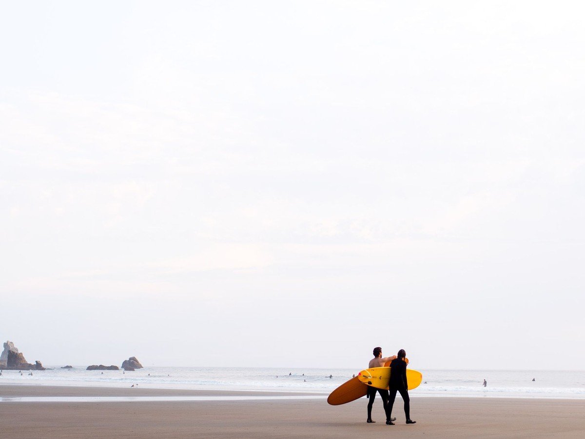 Two surfers walking with their surfboards along a beach at sunrise