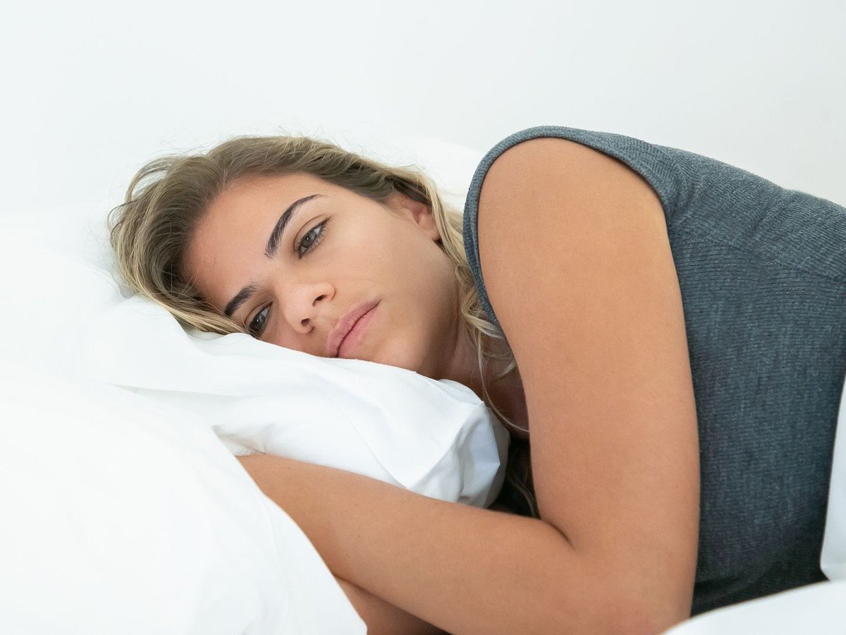 Tired woman lying awake in bed staring at the ceiling —