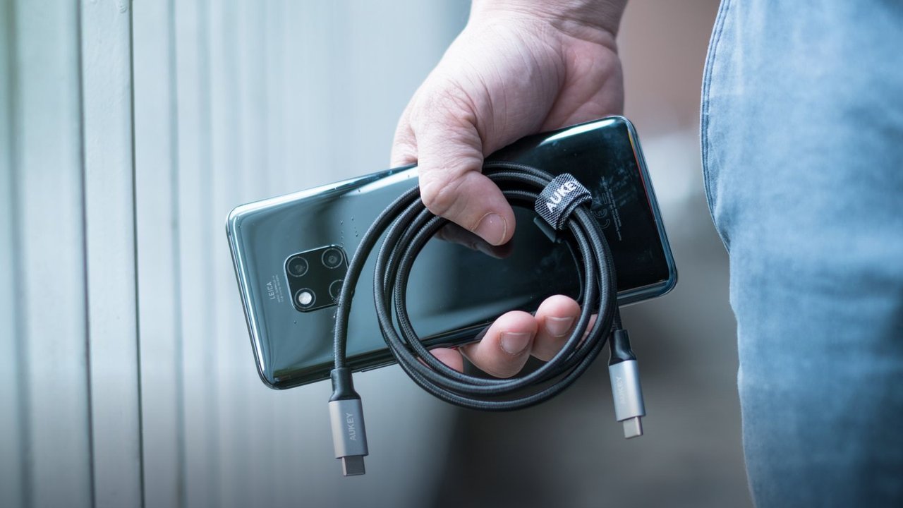 Hand holding a smartphone with a coiled USB cable — use certified chargers for overnight charging
