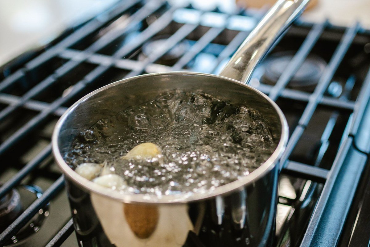 water boiling in a stainless steel pan on a gas stove to loosen burnt food
