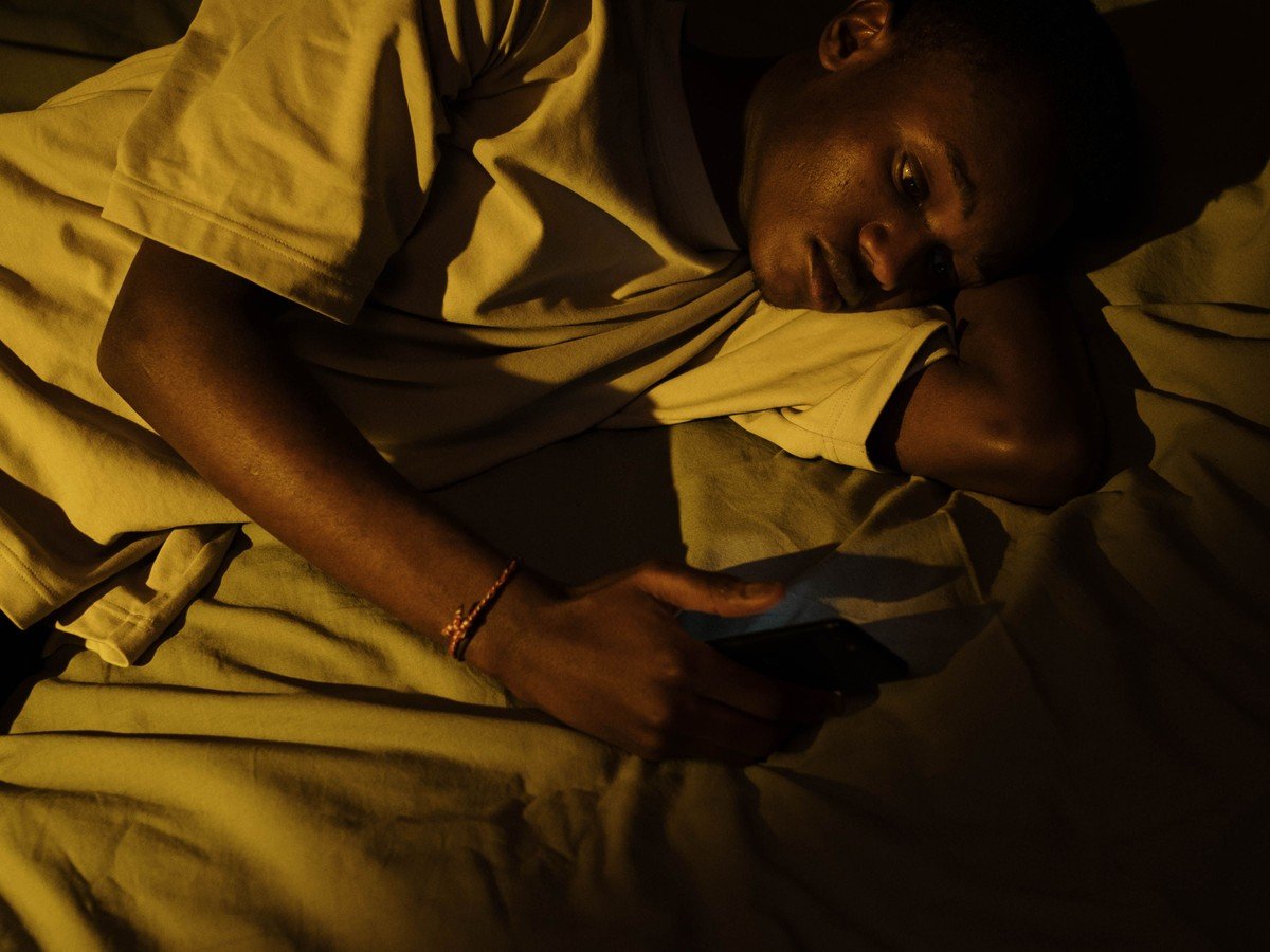 Young man lying awake in bed scrolling on his phone at night — poor sleep habits that worsen snoring