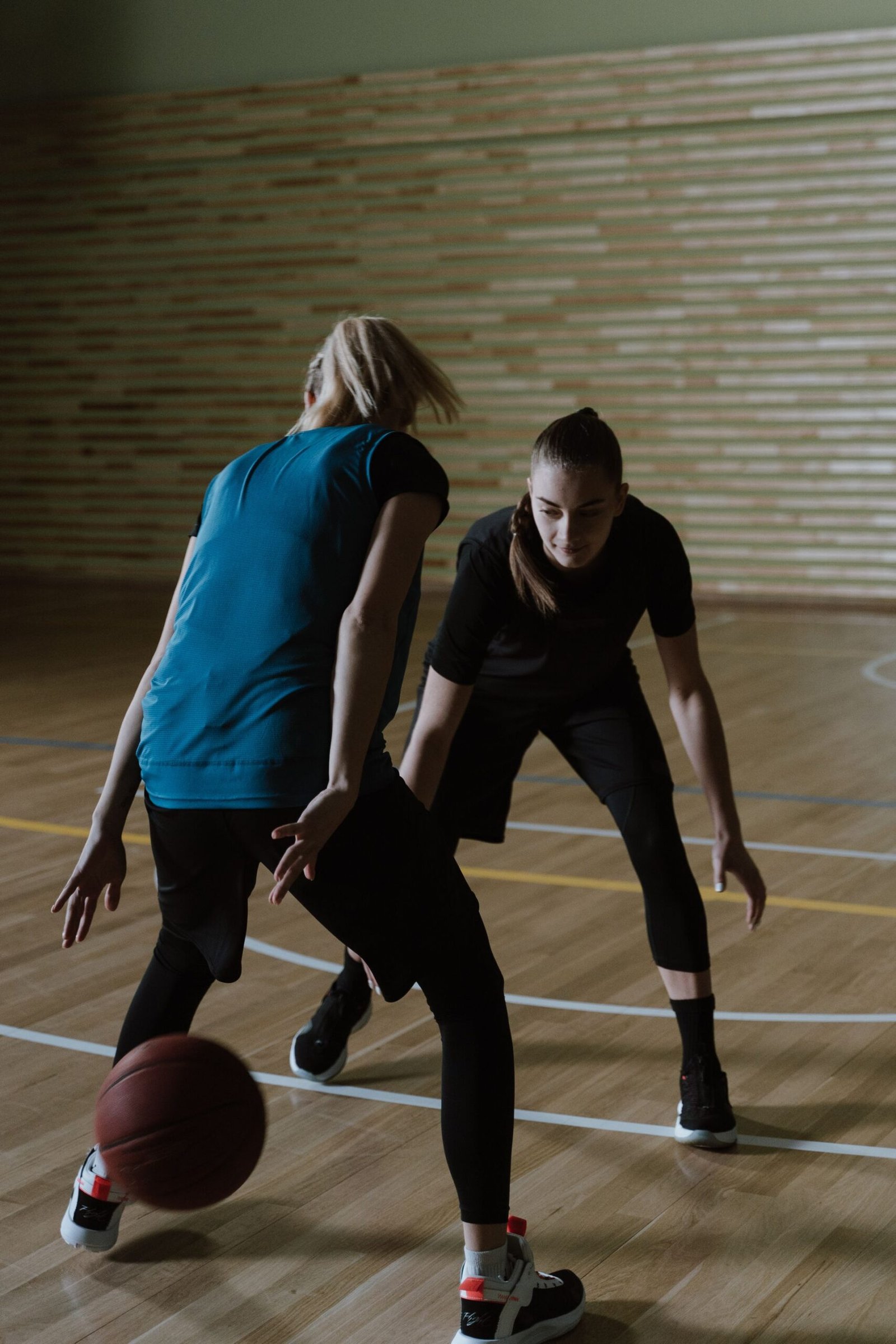 Two women playing an intense indoor basketball game.