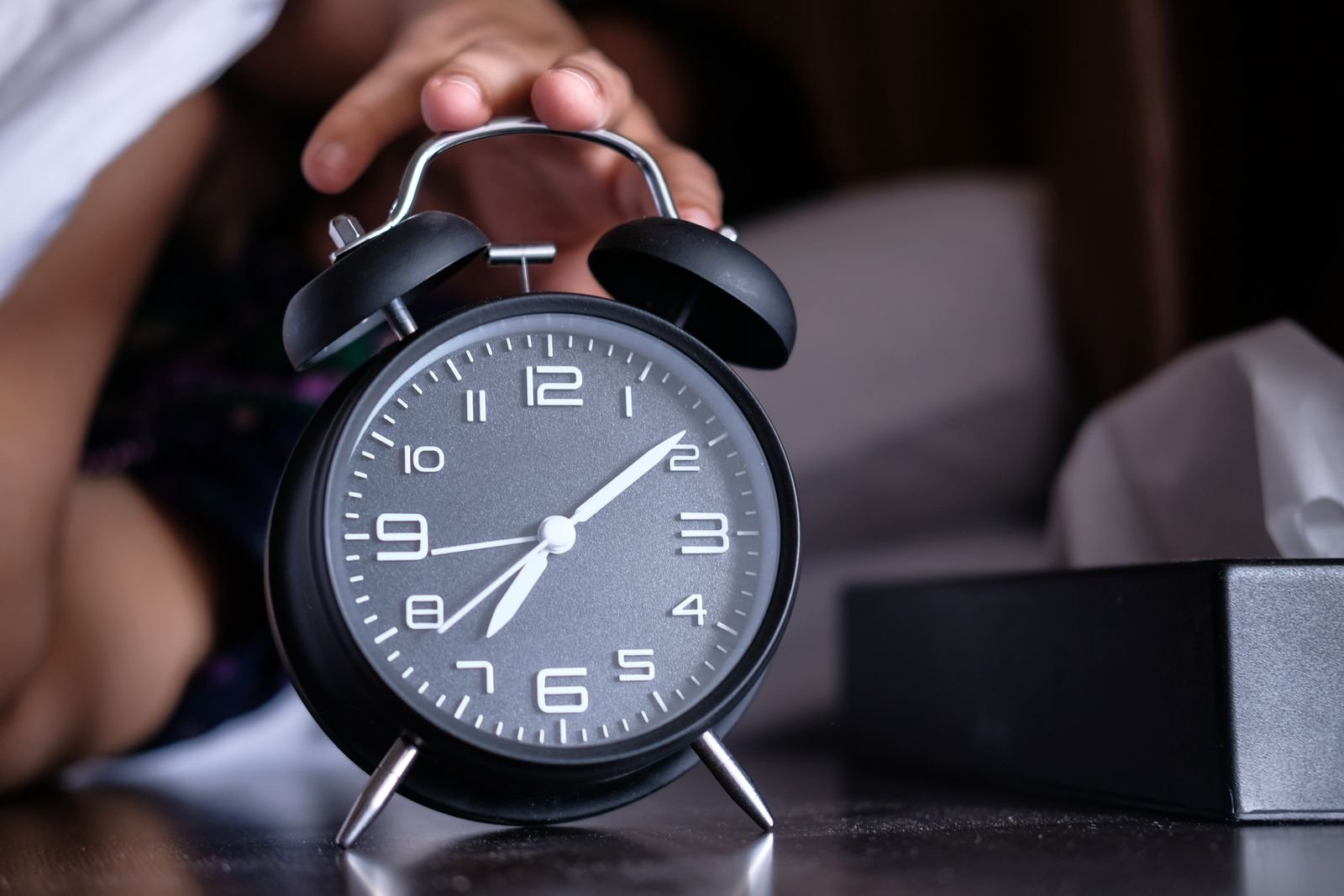 Black alarm clock on a nightstand showing an early morning hour